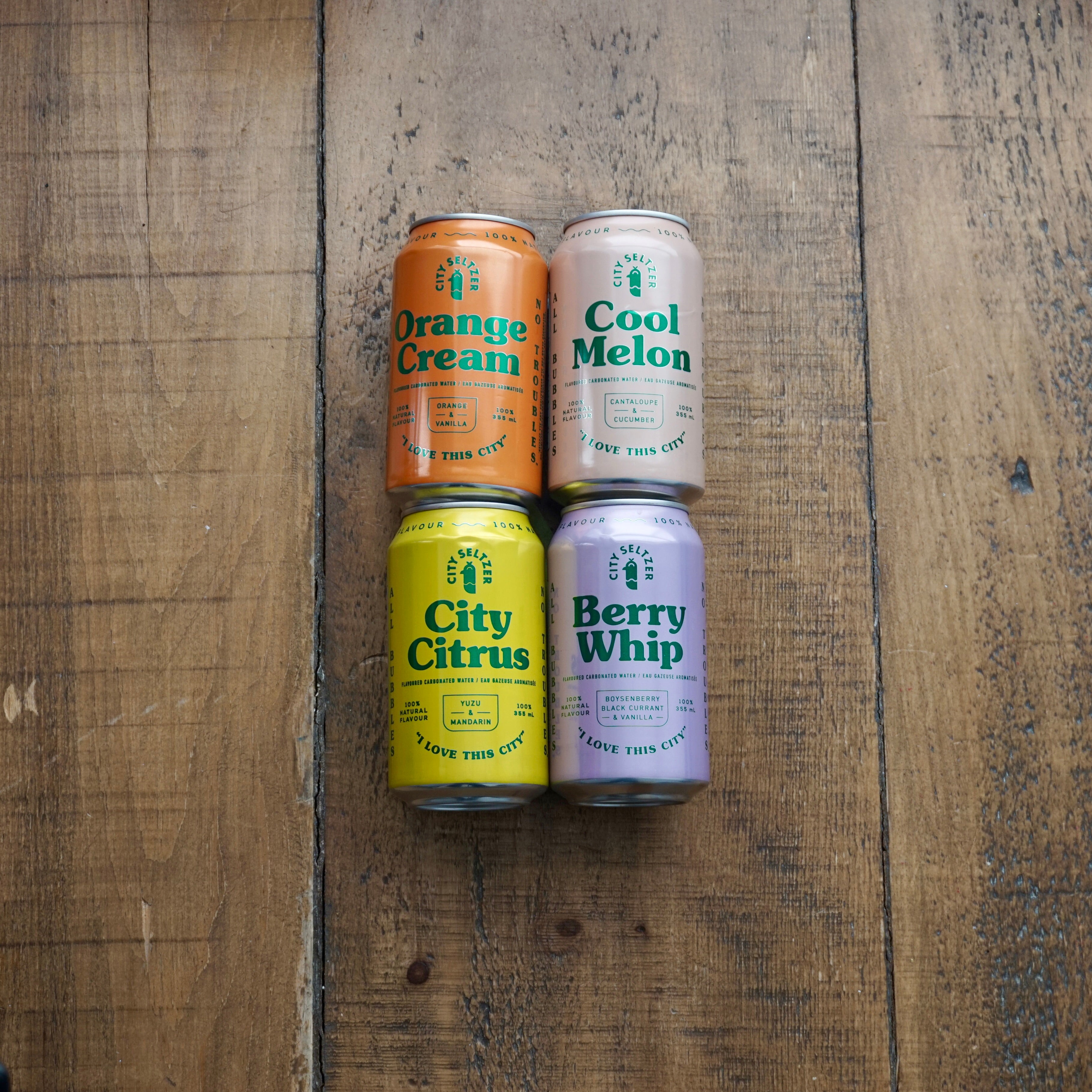 Four canned beverages laid out on a wooden surface, with labels indicating various flavors: Orange Cream, Cool Melon, City Citrus, and Berry Whip.