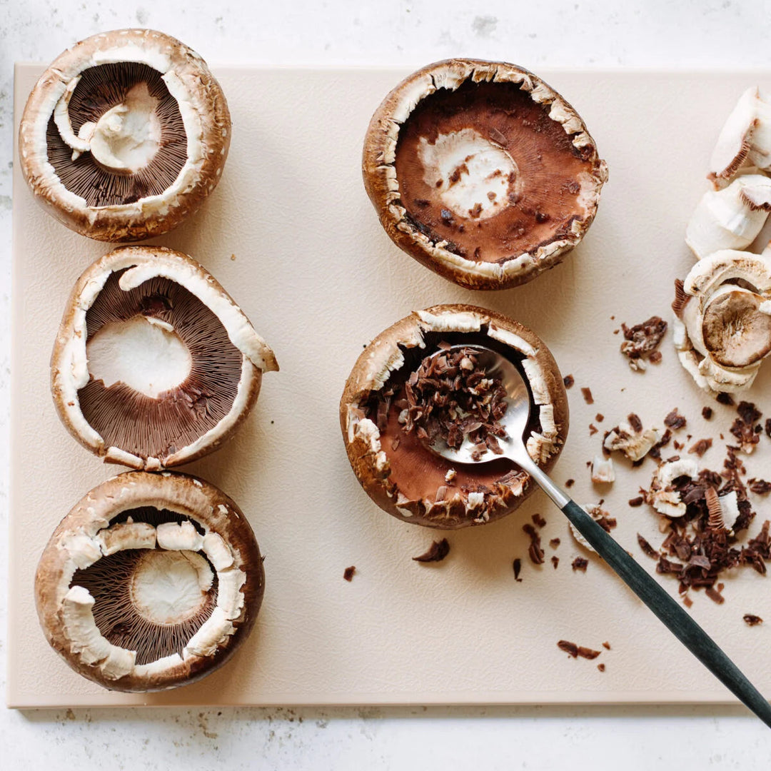 Portobello mushrooms being prepared on a cutting board with a knife.