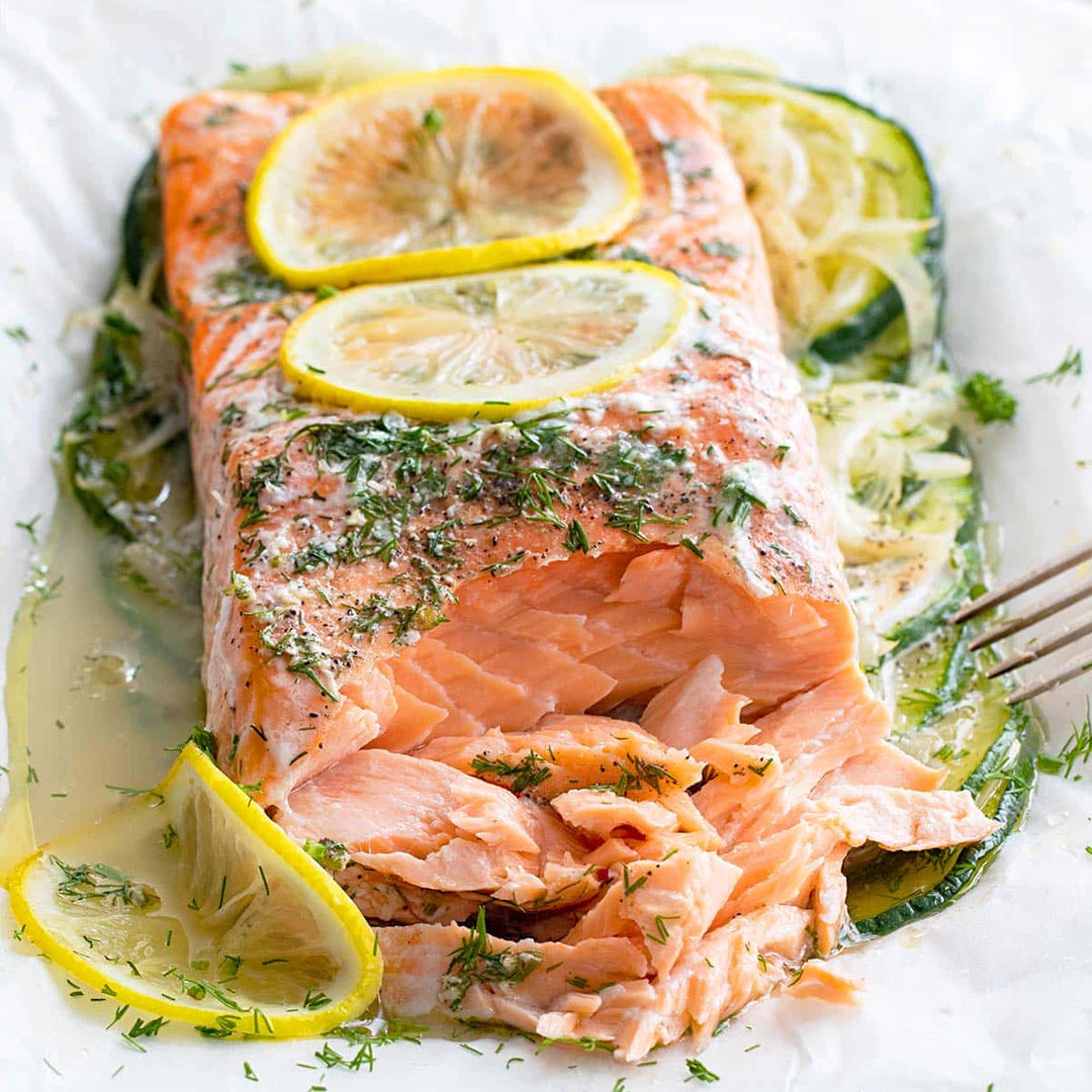 Salmon fillet with lemon slices on a bed of zucchini on a white plate.