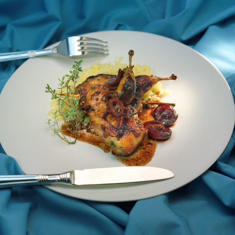 Plated dish of roasted quail with herbs on a white plate with a blue fabric background