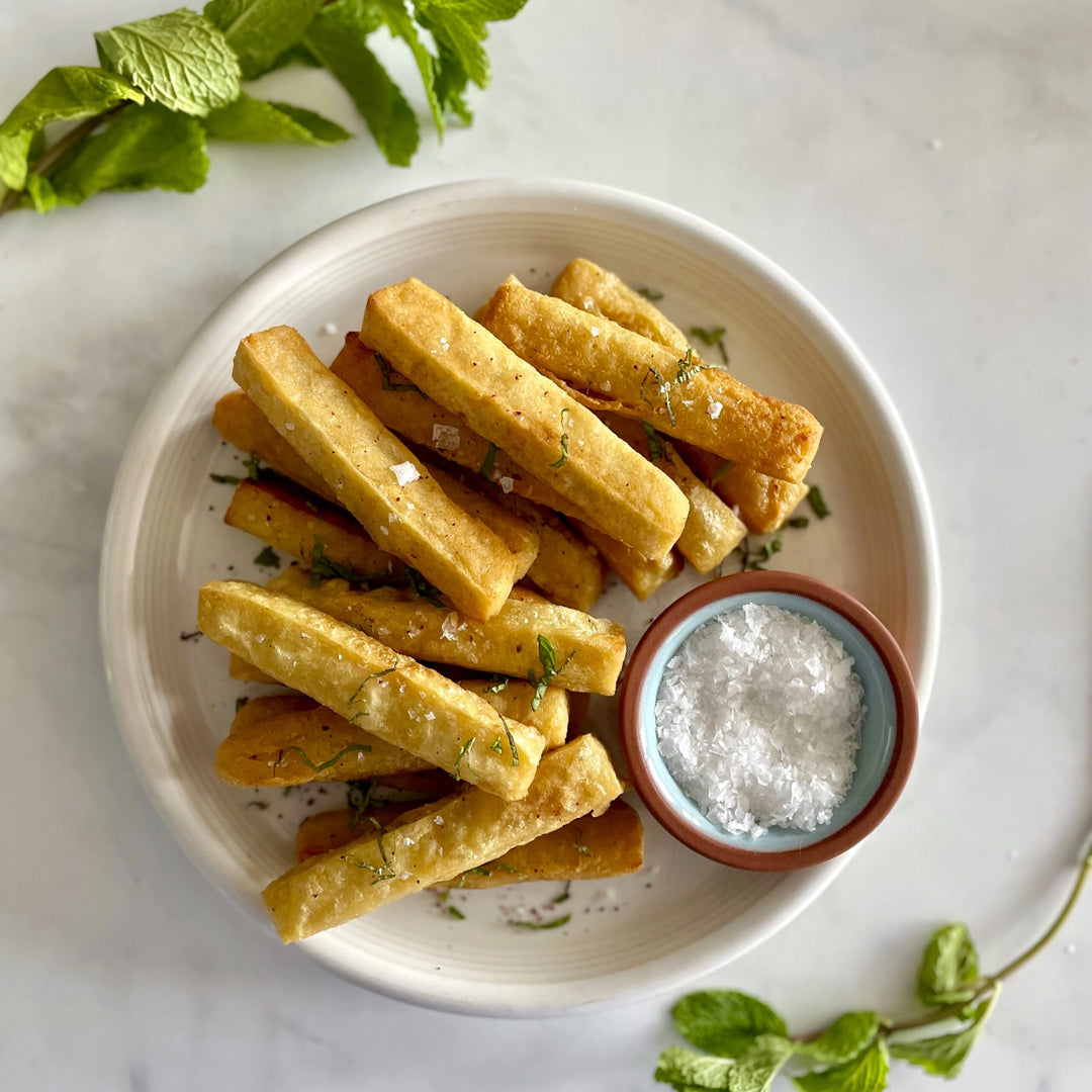 Plate of golden-brown chickpea fries with a small bowl of salt on a light background