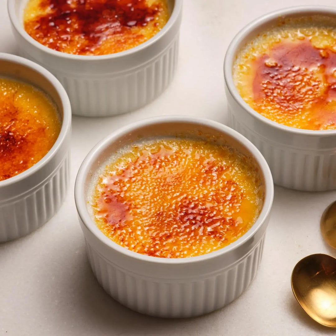 Multiple ramekins of crème bréleé with a golden top on a light background.