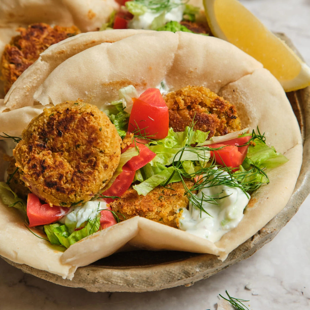 Pita bread with falafel, vegetables, and a side of tzatziki on a marble surface.