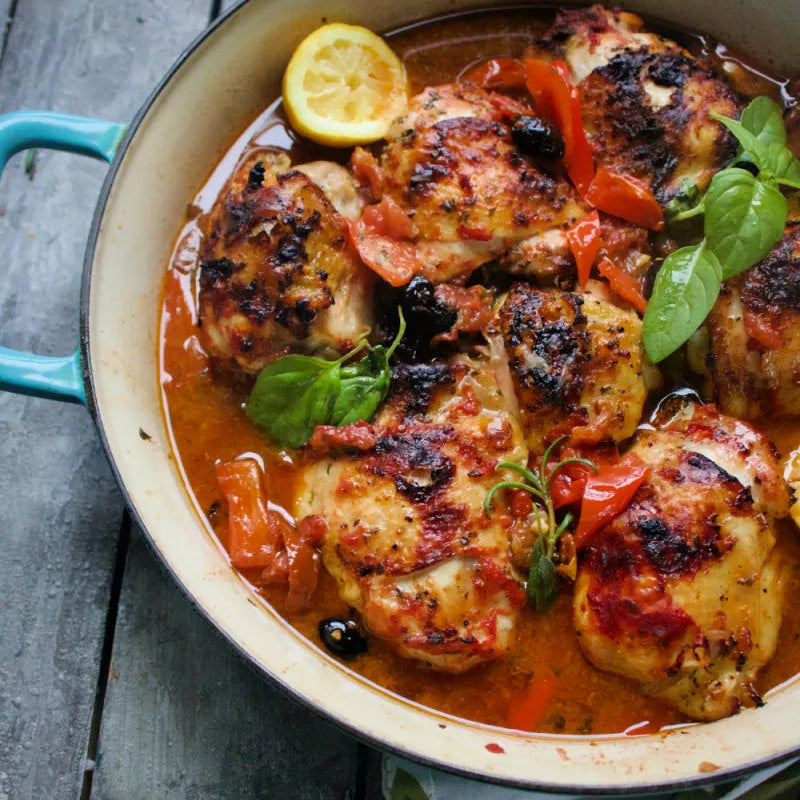 Chicken dish with lemon and herbs in a pan on a wooden table