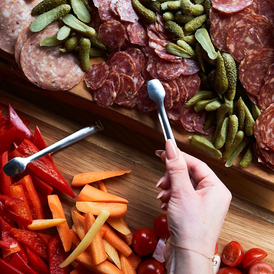 a hand uses a catering pincer to pick up locally made salamis from a charcuterie board made by urban element.