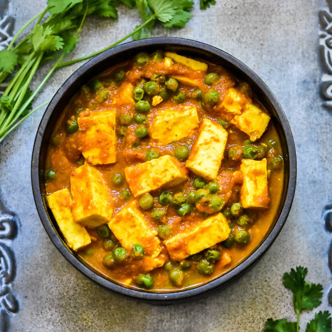 matar paneer dish with paneer and peas in a black bowl on a textured surface with cilantro.