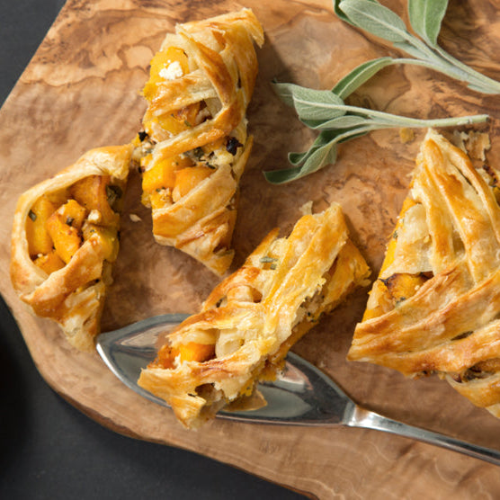 Vegetarian strudel pastry dish with a lattice top on a wooden board with a green plate in the corner.